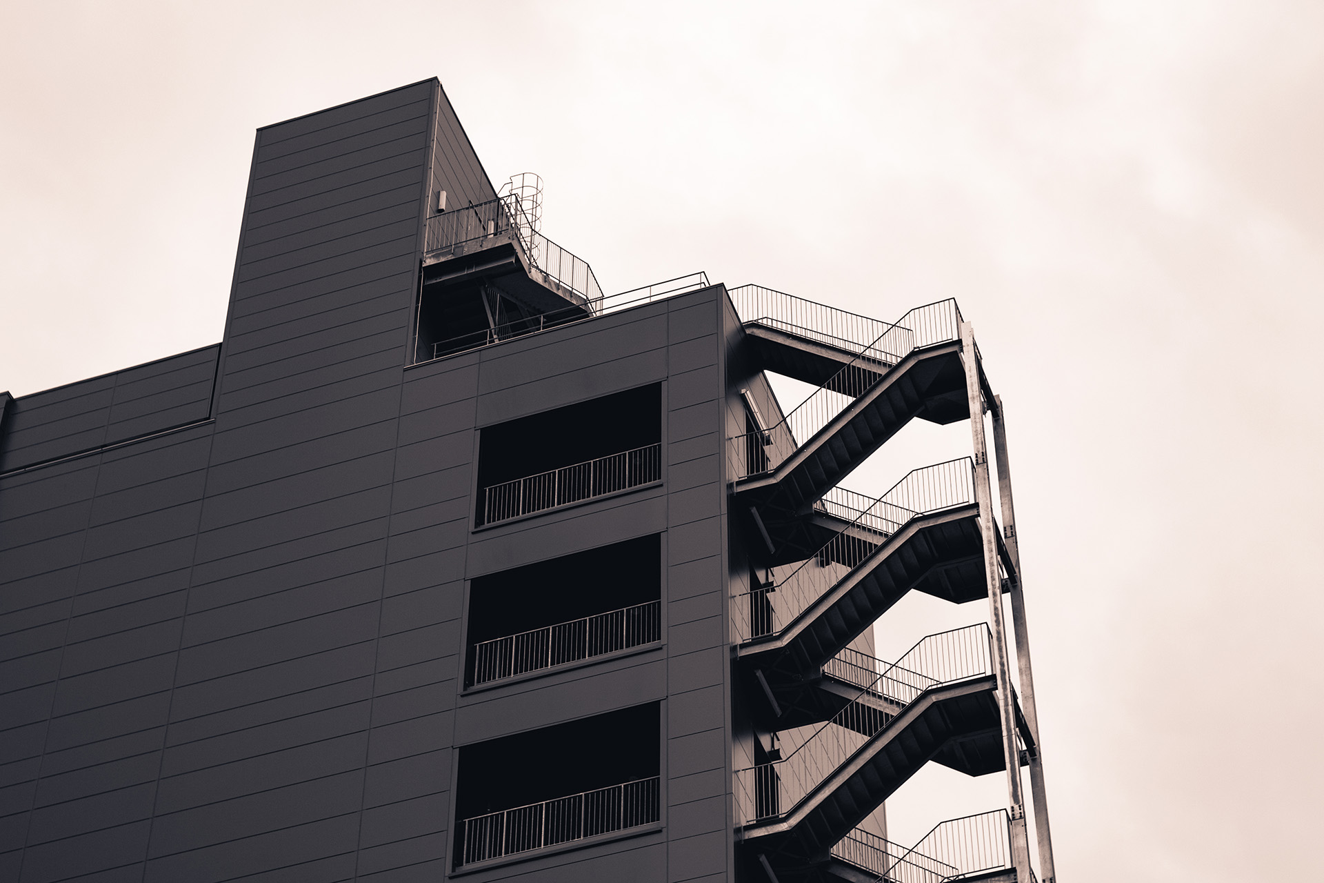 Dark and slick building roof and exterior staircase seen from below with the dark orange sky behind it.